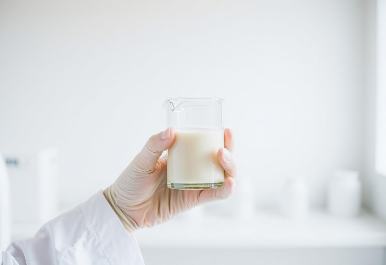 Laborhand hält ein Becherglas mit Milchprobe – Qualitätskontrolle der Babynahrung